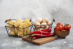 Pasta surrounded by fresh tomato and onion on a rustic wooden table.